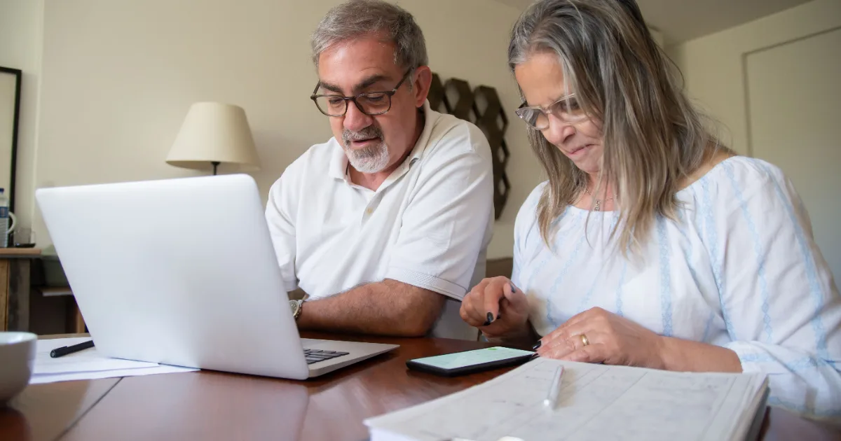 A senior couple reviewing their household budget and projected 2027 Medicare Part B premiums on a laptop with financial documents at home.
