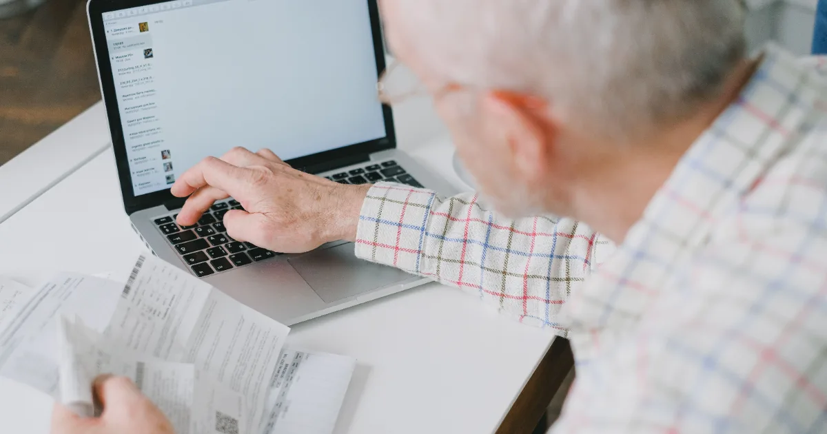 A senior man in a plaid shirt reviewing tax documents and using a laptop to calculate Social Security combined income taxes